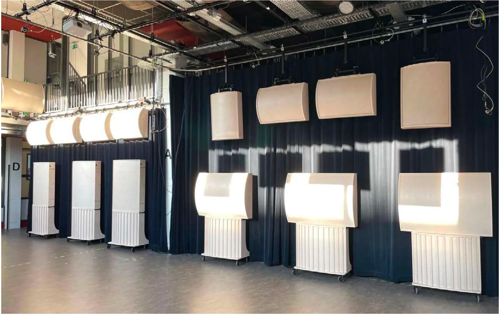 hanging and floor-standing panels in front of a dark curtain, in a room with a high ceiling